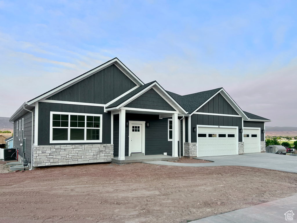 View of front of property with stone siding, an attached garage, driveway, and board and batten siding