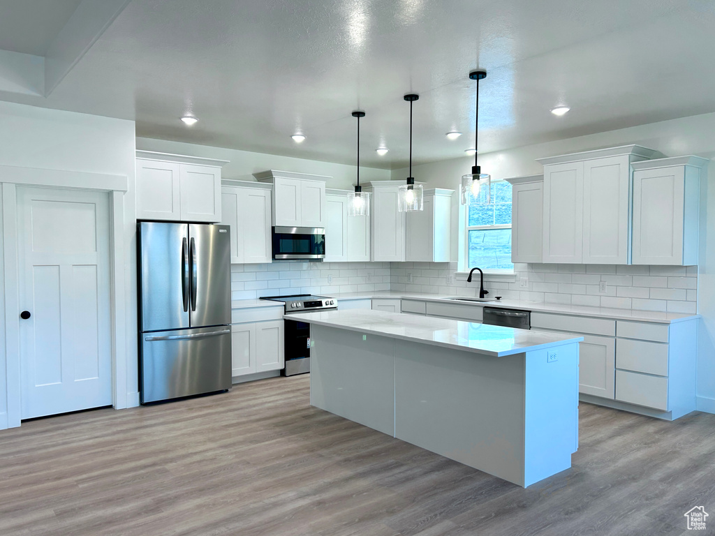 Kitchen with stainless steel appliances, a center island, light countertops, white cabinets, and recessed lighting