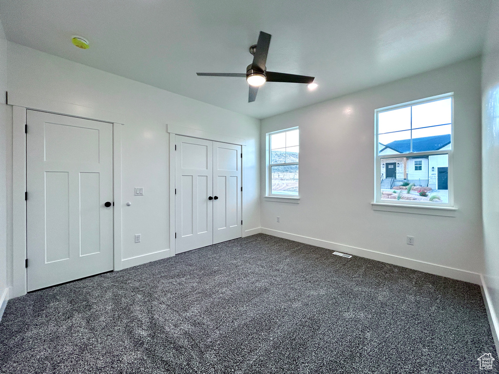 Unfurnished bedroom with dark carpet, a ceiling fan, and multiple closets