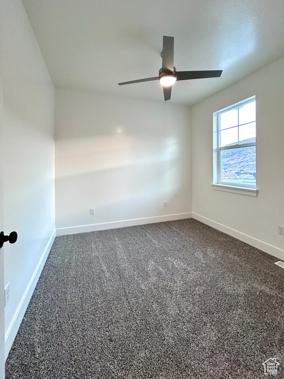 Empty room featuring a ceiling fan and dark colored carpet