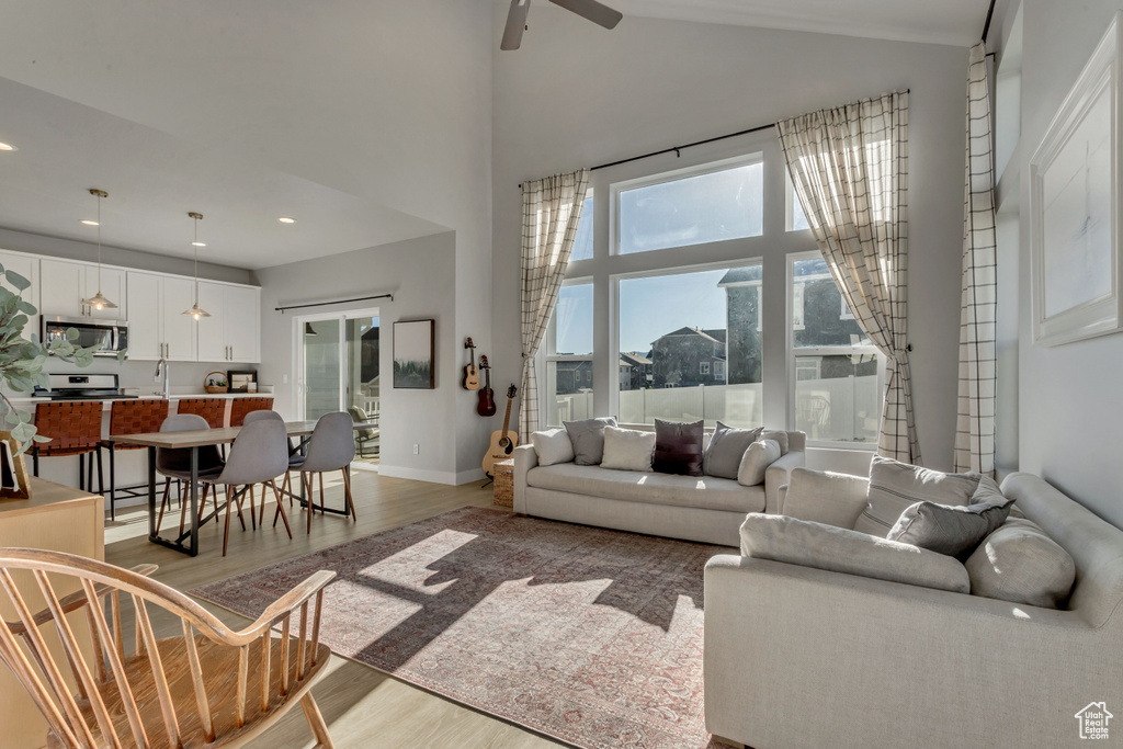 Living room with light wood-type flooring, ceiling fan, high vaulted ceiling, and recessed lighting