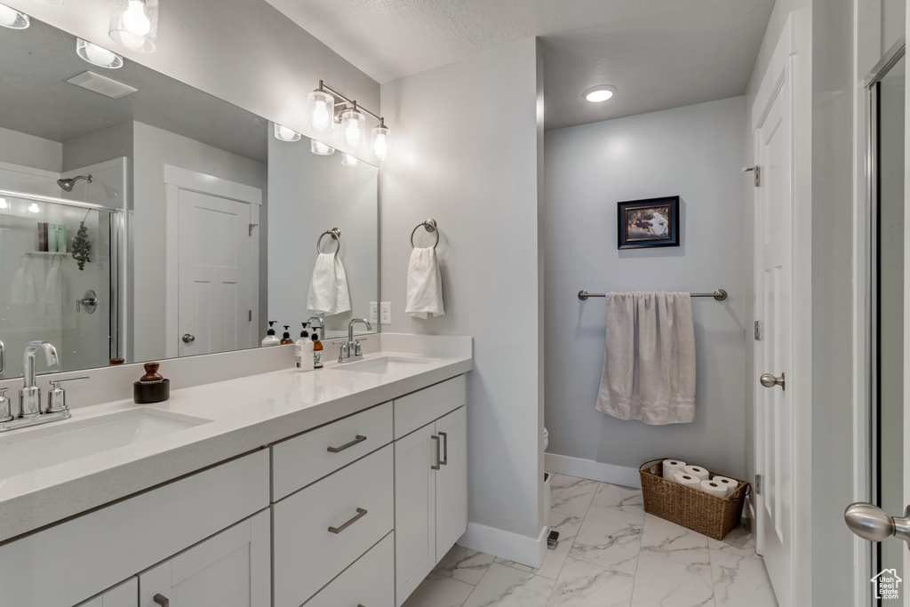 Bathroom featuring double vanity, a shower stall, marble look tile flooring, and recessed lighting