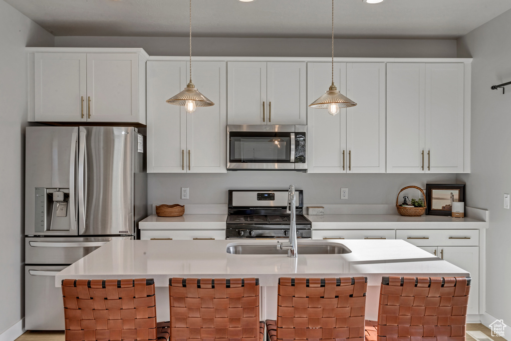 Kitchen featuring stainless steel appliances, a center island with sink, decorative light fixtures, and white cabinets