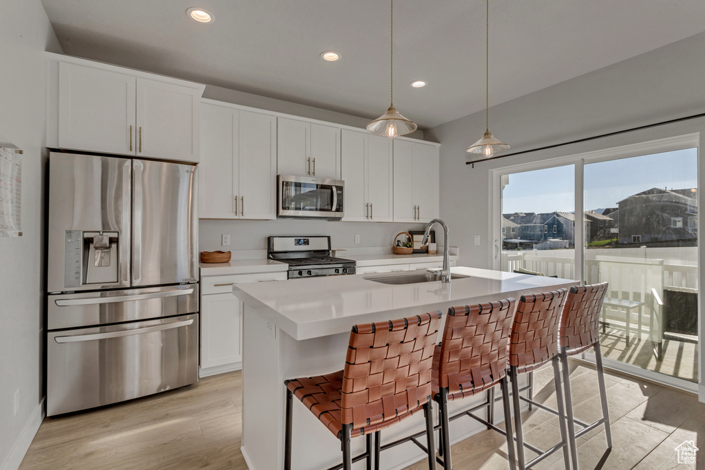 Kitchen with appliances with stainless steel finishes, light countertops, white cabinetry, a kitchen island with sink, and light wood finished floors