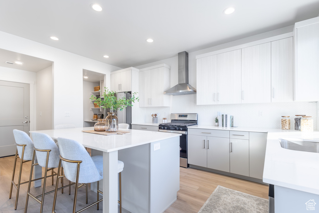 Kitchen with wall chimney range hood, appliances with stainless steel finishes, a kitchen island, a breakfast bar area, and light wood-type flooring