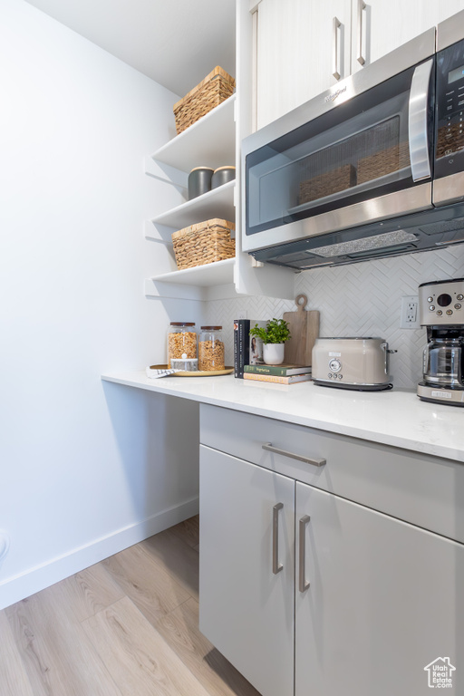 Kitchen featuring stainless steel microwave, open shelves, backsplash, light countertops, and light wood-style floors