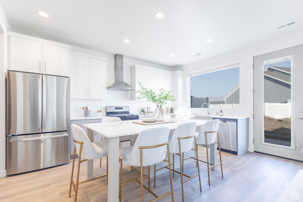 Kitchen with stainless steel appliances, wall chimney range hood, a center island, a kitchen bar, and light countertops