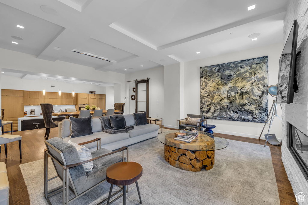 Living area with a barn door, wood finished floors, a large fireplace, recessed lighting, and beamed ceiling