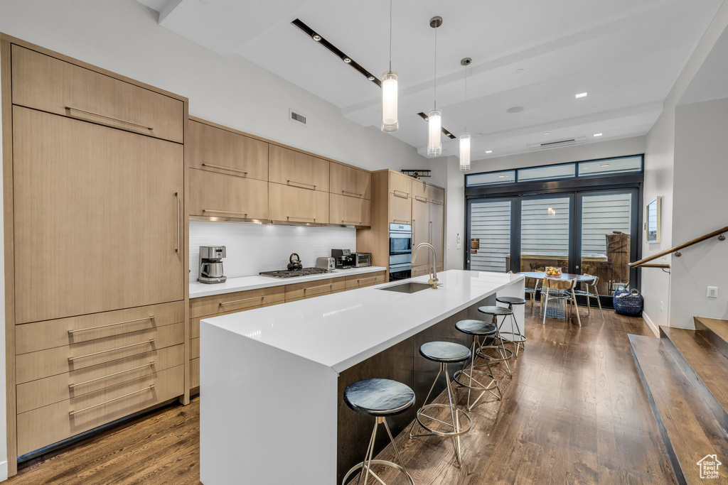 Kitchen featuring a breakfast bar area, dark wood finished floors, light countertops, a kitchen island with sink, and light brown cabinets