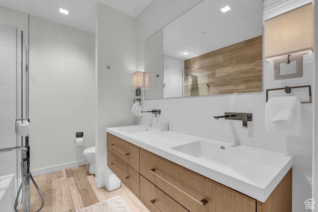 Full bathroom featuring double vanity, backsplash, wood finished floors, and tiled shower