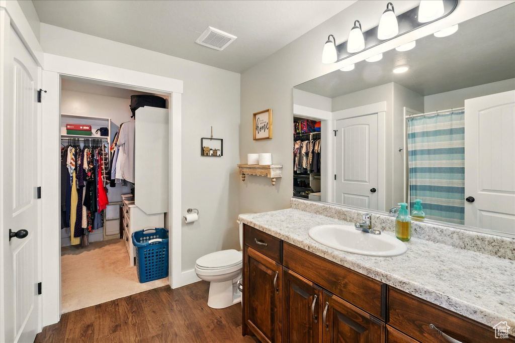 Bathroom featuring a walk in closet, vanity, wood finished floors, and curtained shower