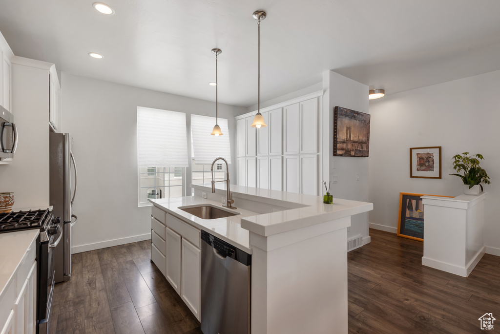 Kitchen with appliances with stainless steel finishes, dark wood finished floors, a kitchen island with sink, white cabinetry, and recessed lighting
