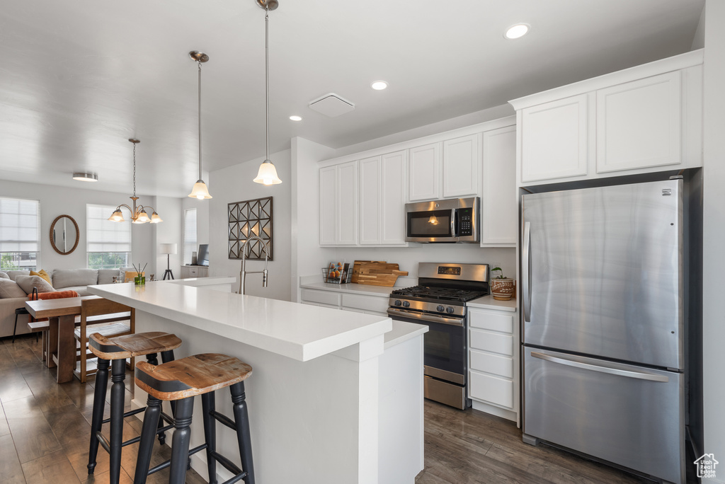 Kitchen featuring appliances with stainless steel finishes, dark wood-style flooring, white cabinets, open floor plan, and a kitchen island