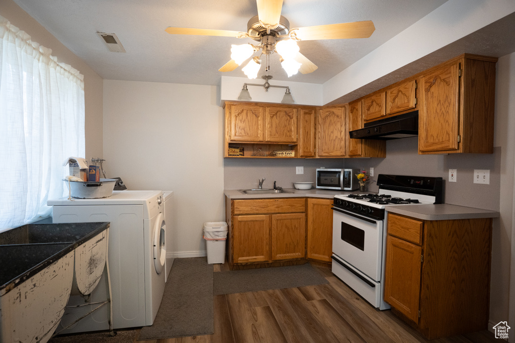 Kitchen with white gas stove, stainless steel microwave, under cabinet range hood, washer / clothes dryer, and dark wood-type flooring