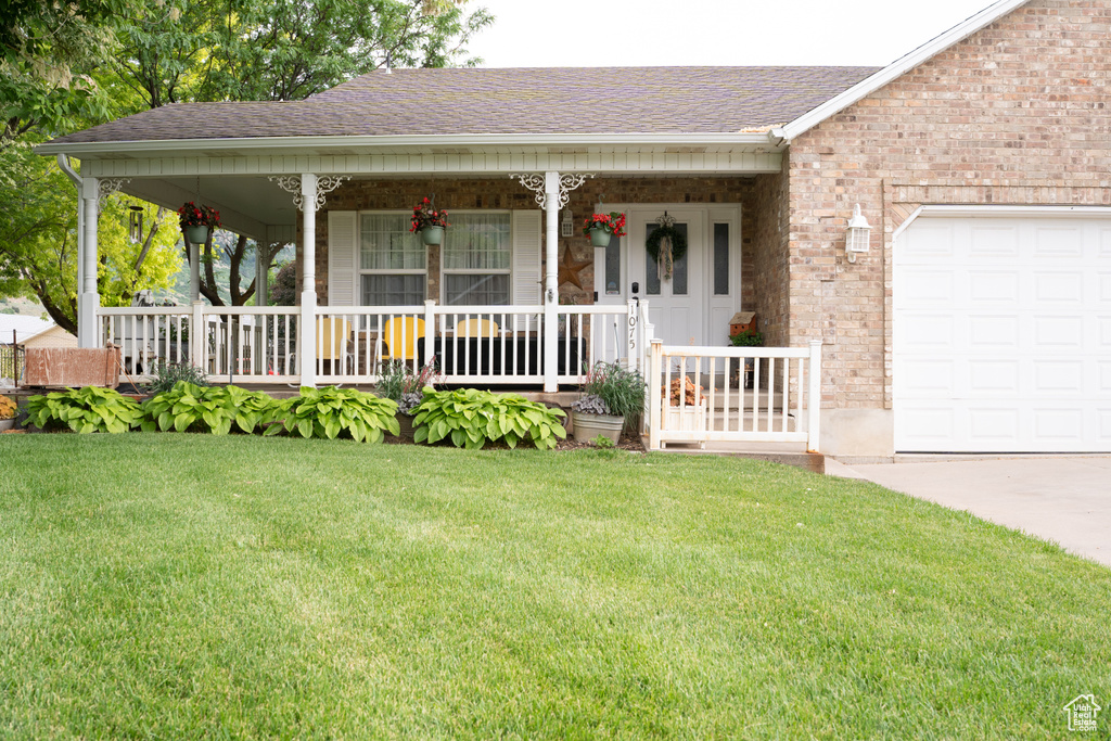 View of front facade with covered porch, a front lawn, roof with shingles, a garage, and concrete driveway