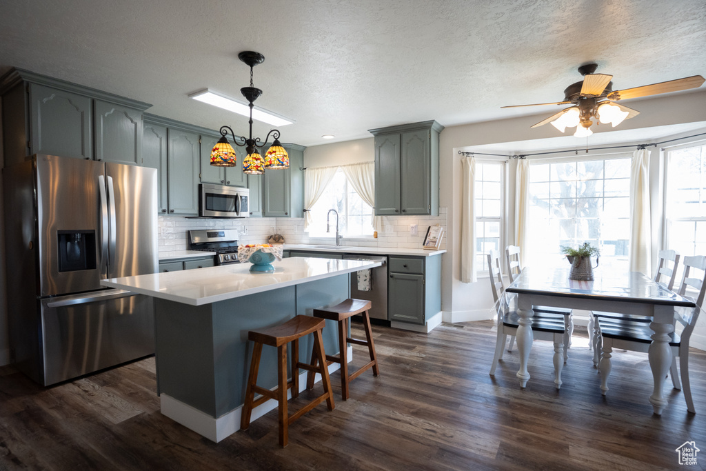 Kitchen with stainless steel appliances, dark wood-type flooring, light countertops, tasteful backsplash, and a center island