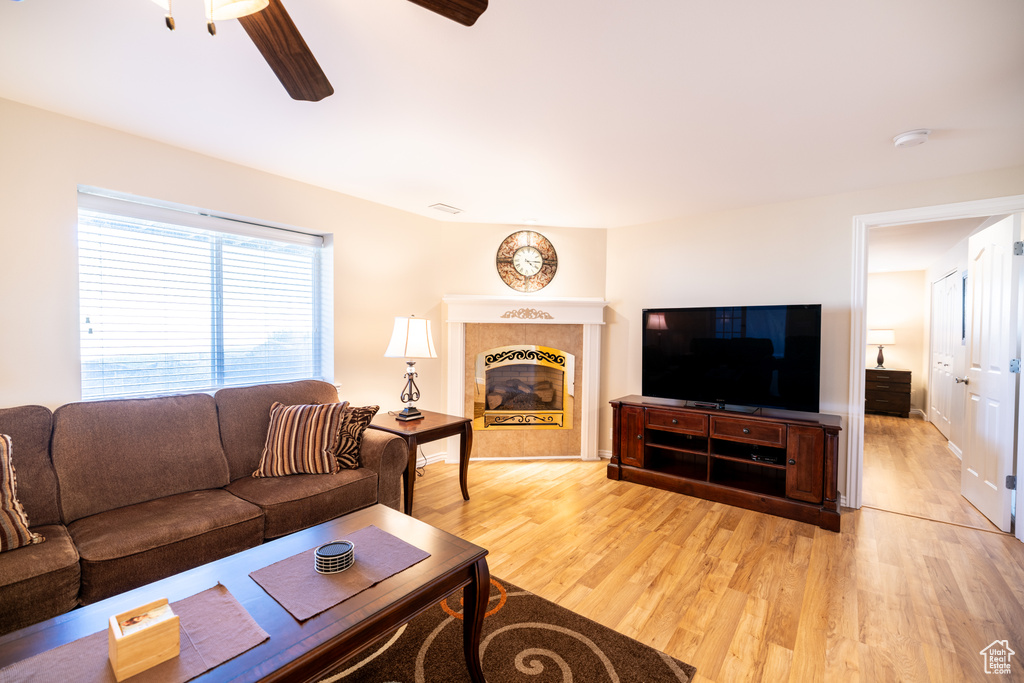 Living area with light wood-style flooring, ceiling fan, and a tile fireplace