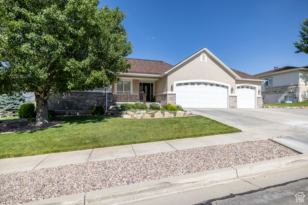 Ranch-style house featuring a garage, stucco siding, a front yard, and driveway