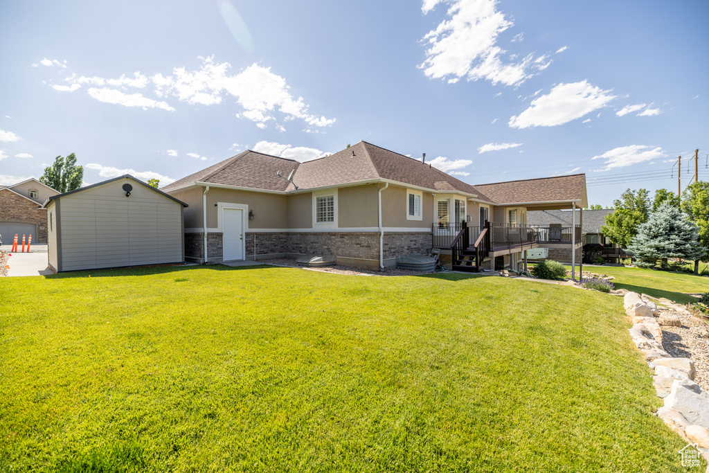 Back of property with stucco siding, a yard, a shingled roof, a storage unit, and a wooden deck