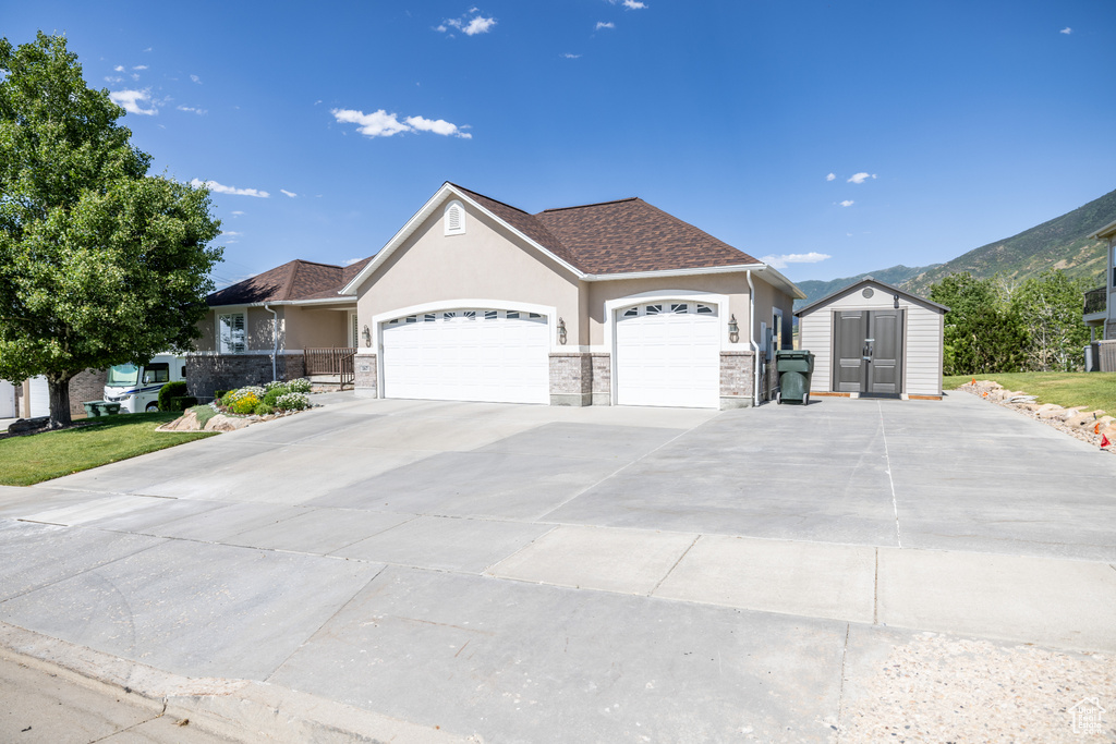 Single story home featuring a shed, stucco siding, an attached garage, driveway, and a mountain view