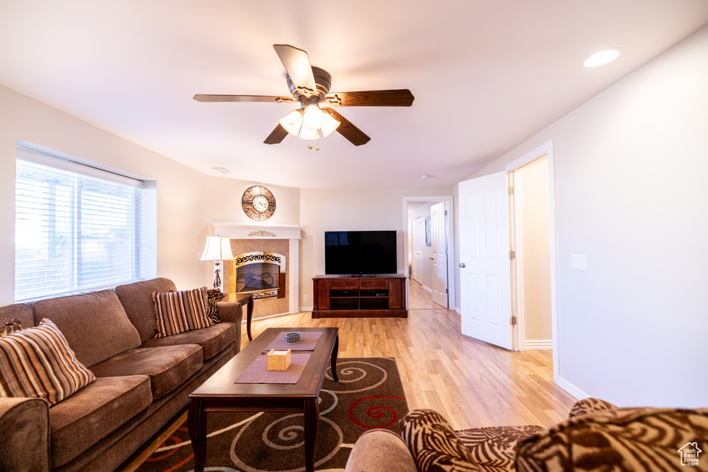 Living room featuring light wood-type flooring, ceiling fan, and a fireplace