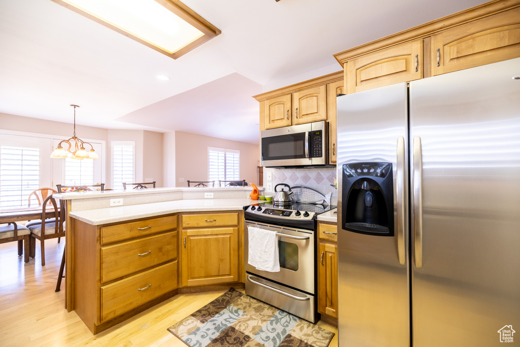 Kitchen featuring stainless steel appliances, a peninsula, light countertops, tasteful backsplash, and light wood-style flooring