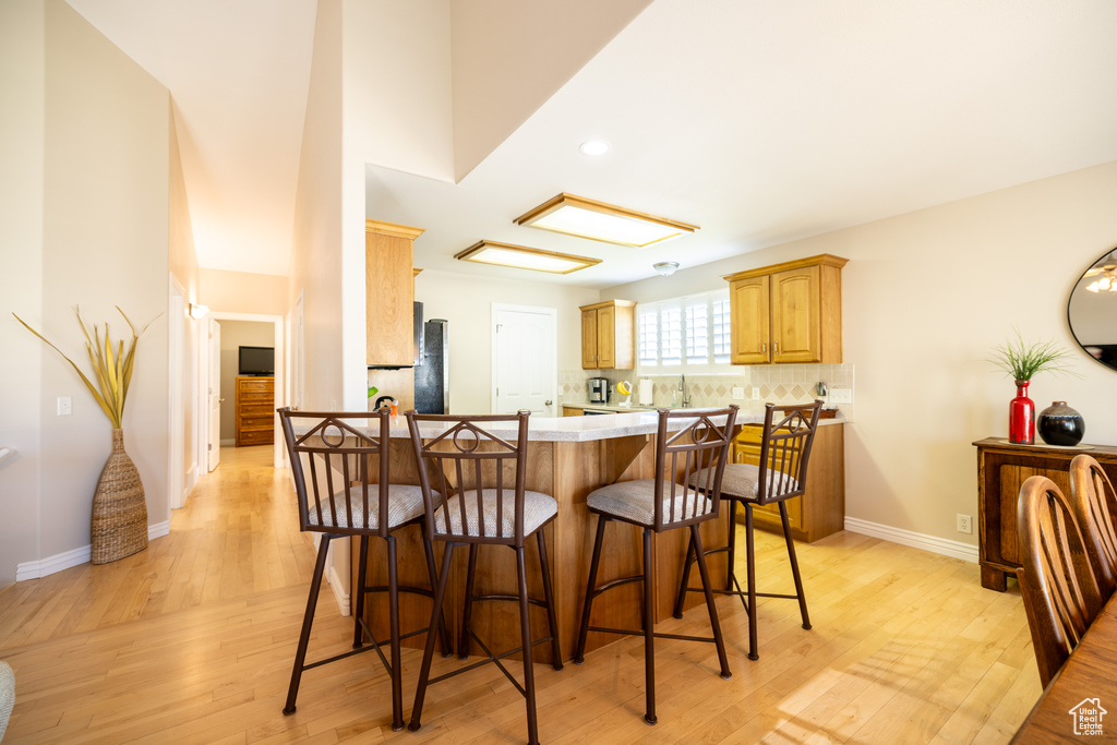 Kitchen featuring a breakfast bar area, light wood-type flooring, light countertops, tasteful backsplash, and recessed lighting