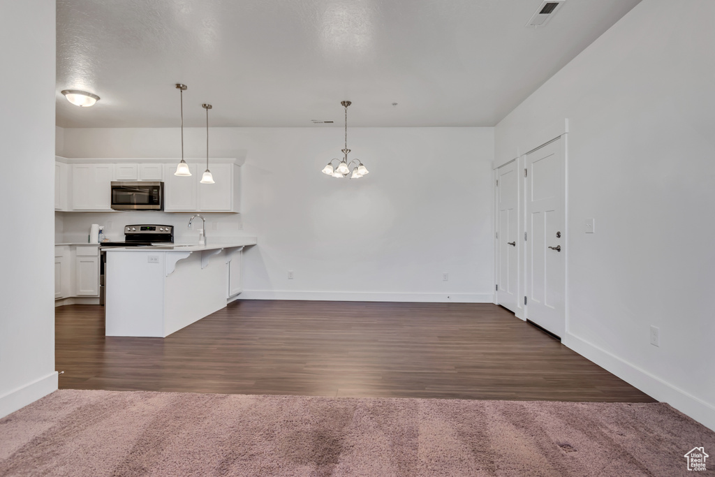 Kitchen featuring appliances with stainless steel finishes, a kitchen bar, white cabinets, a peninsula, and hanging light fixtures