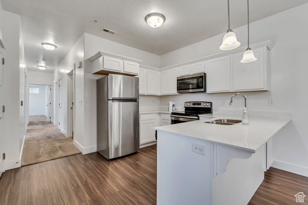 Kitchen featuring appliances with stainless steel finishes, a peninsula, dark wood finished floors, and white cabinets