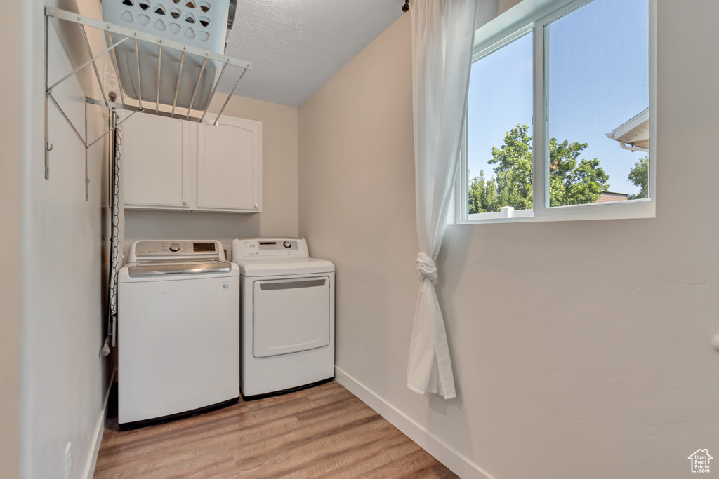 Laundry area with separate washer and dryer, light wood finished floors, and cabinet space