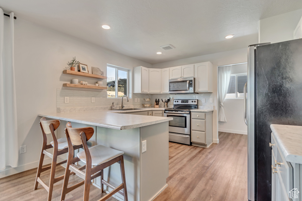 Kitchen featuring appliances with stainless steel finishes, a peninsula, backsplash, light wood-type flooring, and recessed lighting