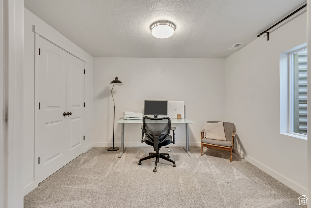 Carpeted office space with a textured ceiling and baseboards