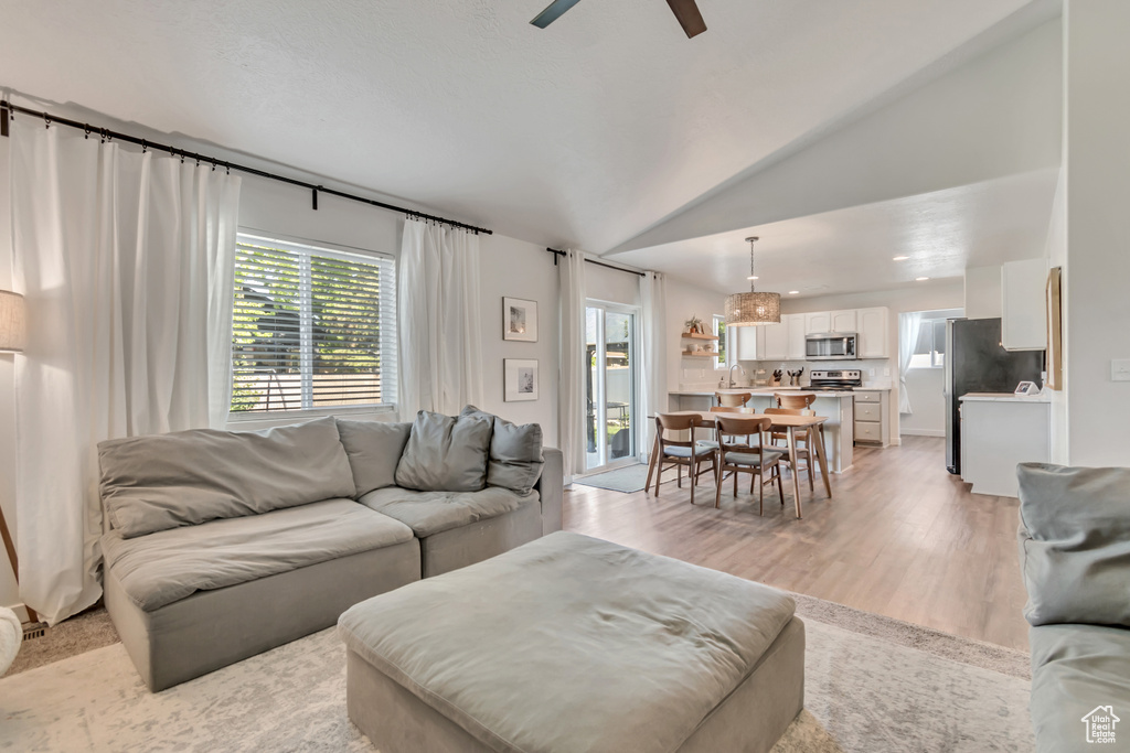 Living area featuring plenty of natural light, a ceiling fan, light wood-style flooring, and lofted ceiling