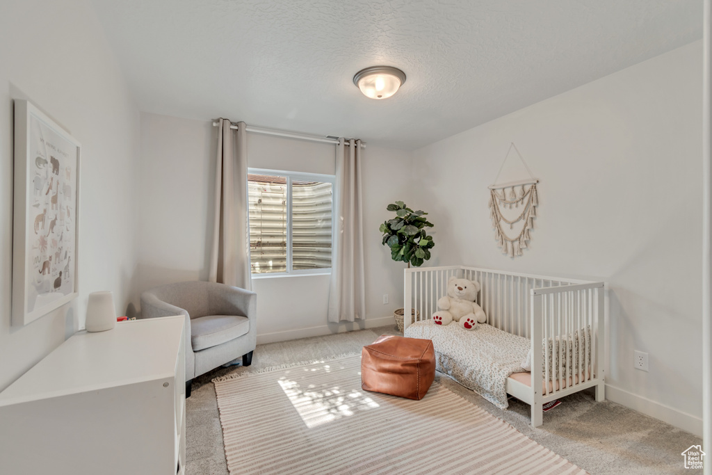 Bedroom with carpet flooring, a textured ceiling, and a nursery area