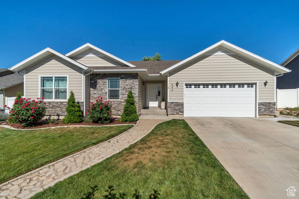 Craftsman inspired home with a garage, stone siding, a front lawn, and concrete driveway