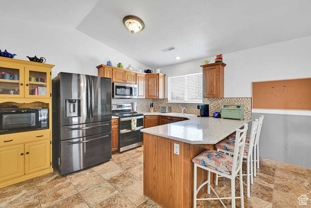 Kitchen with appliances with stainless steel finishes, a peninsula, backsplash, stone tile floors, and lofted ceiling