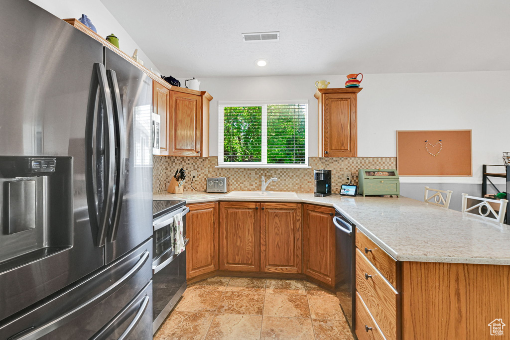 Kitchen featuring appliances with stainless steel finishes, a peninsula, decorative backsplash, and brown cabinets