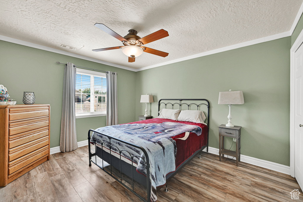 Bedroom with wood finished floors, ornamental molding, a textured ceiling, and a ceiling fan
