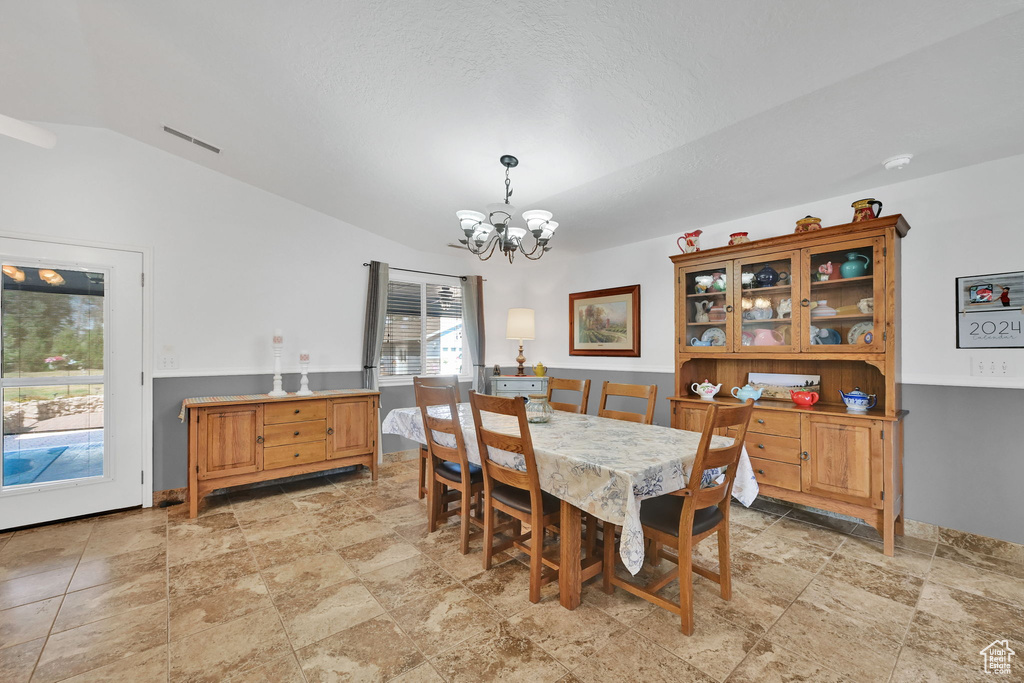 Dining space with a chandelier, light stone finish floors, and lofted ceiling