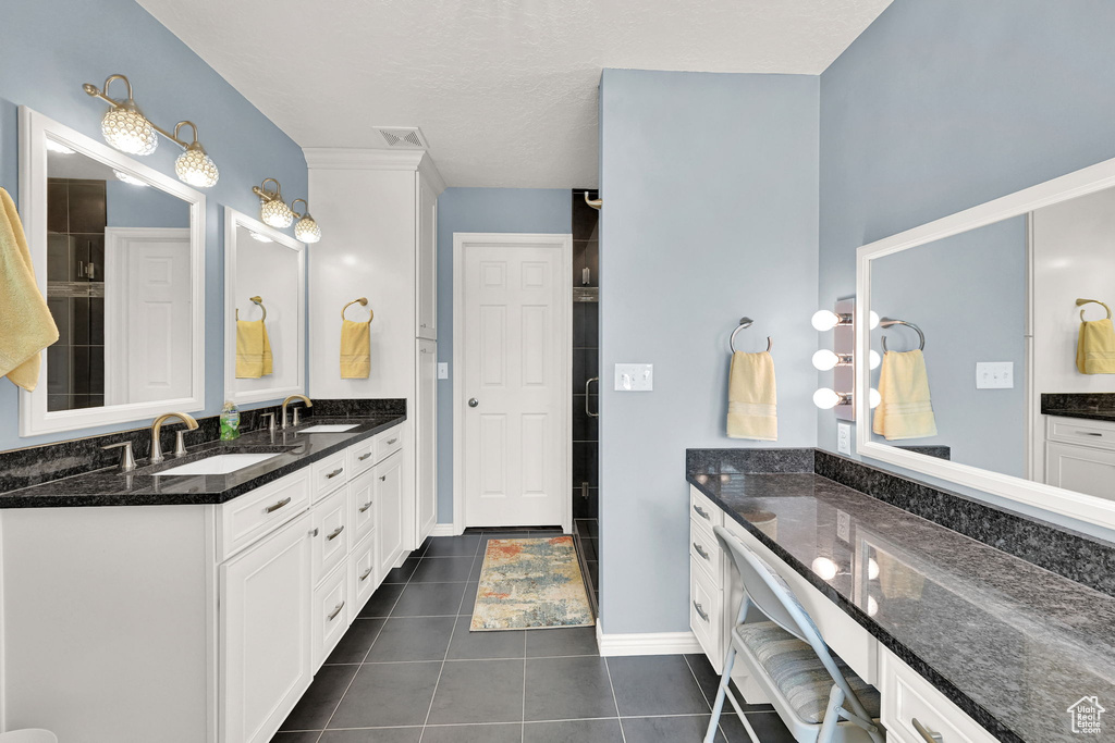 Bathroom with double vanity, tile patterned flooring, and a tile shower