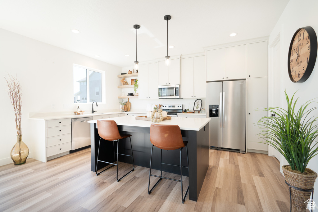 Kitchen featuring appliances with stainless steel finishes, a center island, light wood-style floors, a kitchen breakfast bar, and light countertops