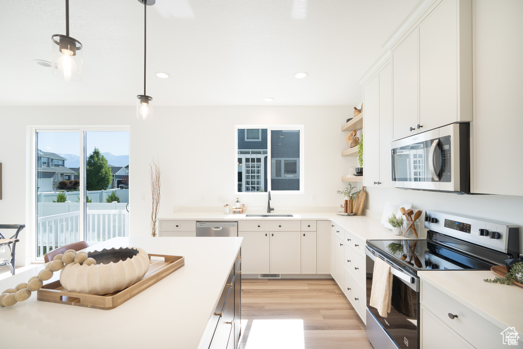 Kitchen featuring stainless steel appliances, light wood-style flooring, white cabinetry, hanging light fixtures, and open shelves
