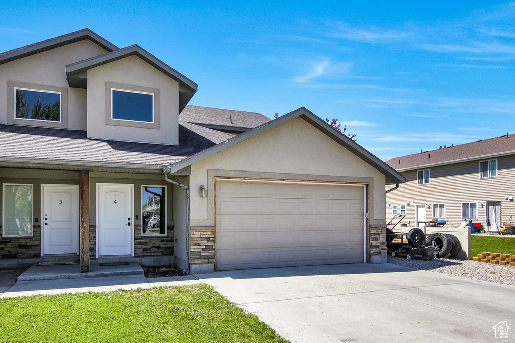 Townhome / multi-family property with stone siding, stucco siding, a garage, driveway, and roof with shingles