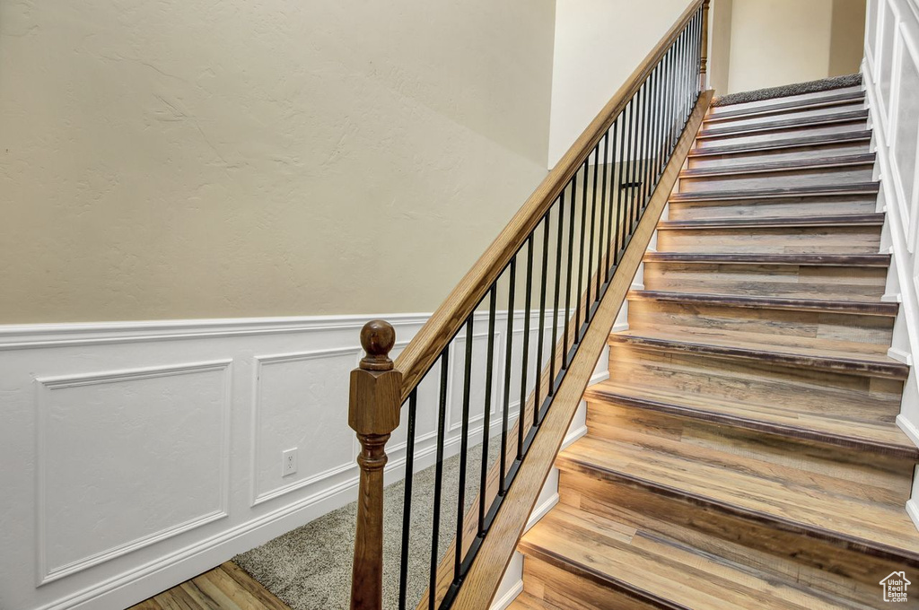 Stairs featuring wainscoting, wood finished floors, and a decorative wall