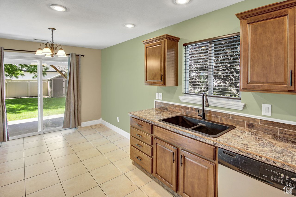 Kitchen featuring dishwashing machine, light tile patterned flooring, hanging light fixtures, stone countertops, and a chandelier