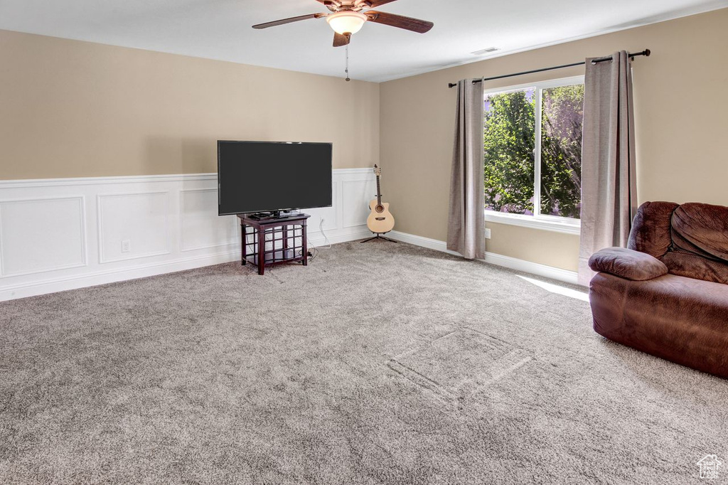 Living area featuring ceiling fan, carpet, and a wainscoted wall