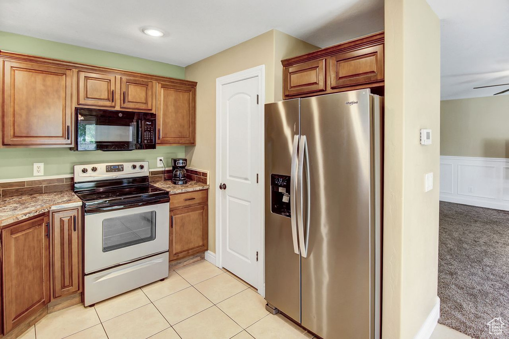 Kitchen with stainless steel appliances, brown cabinetry, stone countertops, and wainscoting