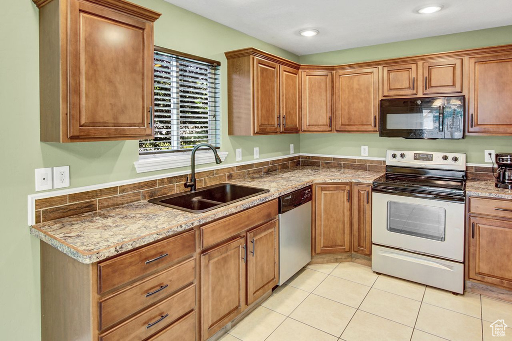 Kitchen with appliances with stainless steel finishes, light tile patterned floors, and brown cabinets