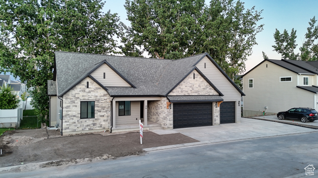View of front facade featuring stone siding, a shingled roof, an attached garage, and concrete driveway