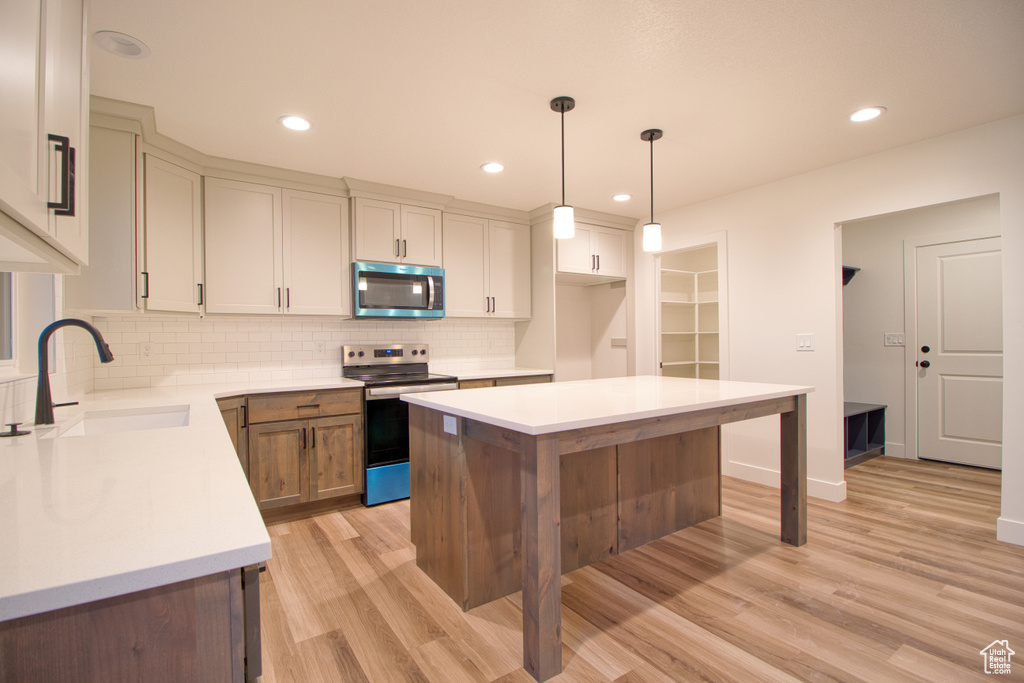 Kitchen with appliances with stainless steel finishes, tasteful backsplash, light wood-style floors, light countertops, and decorative light fixtures